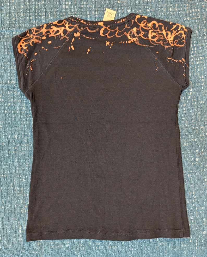 Może przedstawiać: Ciemnoniebieska koszulka z kr&oacute;tkim rękawem. Ramiona i g&oacute;rna część plec&oacute;w mają jasnopomarańczowy wz&oacute;r, ze wzorem rozprysk&oacute;w i fal. Koszulka jest wykonana z miękkiego materiału.