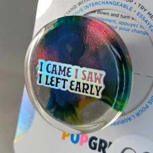 May include: A round, clear glass paperweight with a colorful, abstract design. The paperweight has a sticker on it that says "I came I saw I left early".