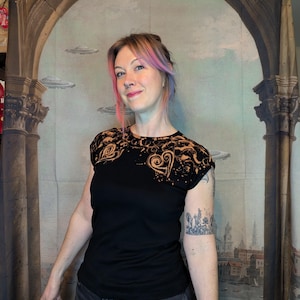 Może przedstawiać: Czarny t-shirt z motywem serca na ramieniu i klatce piersiowej. Wz&oacute;r ma wybielony efekt, tworząc unikalny wz&oacute;r. Modelka ma na sobie ciemne dżinsy i tatuaż na ramieniu.