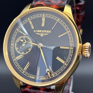 May include: A gold Longines wristwatch with a black face, gold hands and markers, and a small seconds dial. The watch is set on a red leather strap. The watch face displays the Longines logo and the words "SWISS MADE".