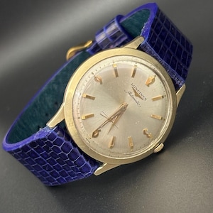 May include: A gold-toned Longines Automatic wristwatch with a silver face and gold hands and markers. The watch has a blue leather band. The watch face displays the Longines logo.