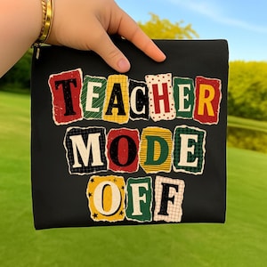 May include: Black zippered pouch with the text "TEACHER MODE OFF" in a colorful, distressed, collage-style design. The text is arranged in three lines, with each word on a separate line. The background is a green field and blue sky.