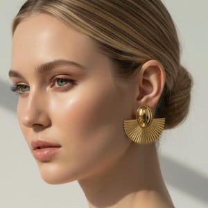 Può includere: Orecchini dorati. Ogni orecchino presenta un design a forma di ventaglio con una superficie strutturata e scanalata. Gli orecchini hanno una chiusura a perno e una finitura lucida.