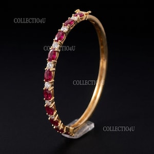 May include: A gold bangle bracelet featuring an alternating pattern of oval-cut red rubies and round-cut clear white stones set in a continuous row. The text COLLECTIO4U is visible in multiple locations on the image background.