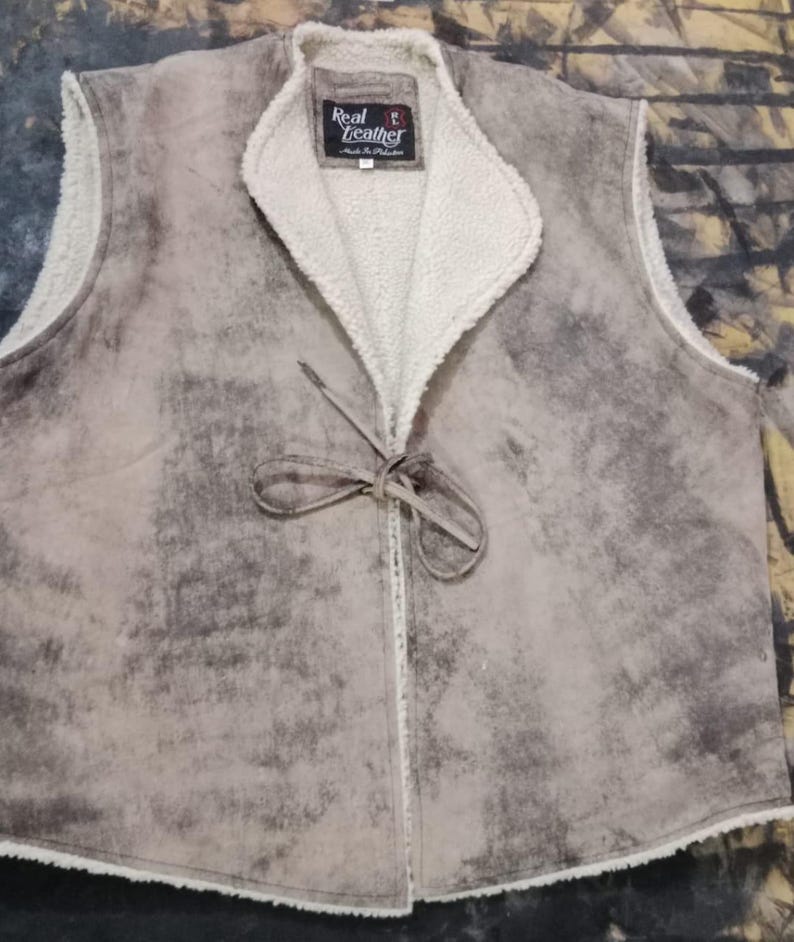 May include: A tan leather vest with a cream-colored, fuzzy lining and collar. The vest has a tie closure and a label that reads "Real Leather". The vest has a distressed, mottled appearance.