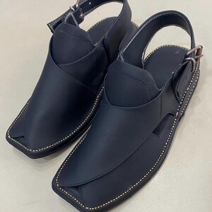 Peut inclure: Une paire de sandales en cuir noir avec un bout carré. Les sandales ont une bride de cheville et sont cousues avec du fil blanc. Les semelles sont cousues avec du fil doré.