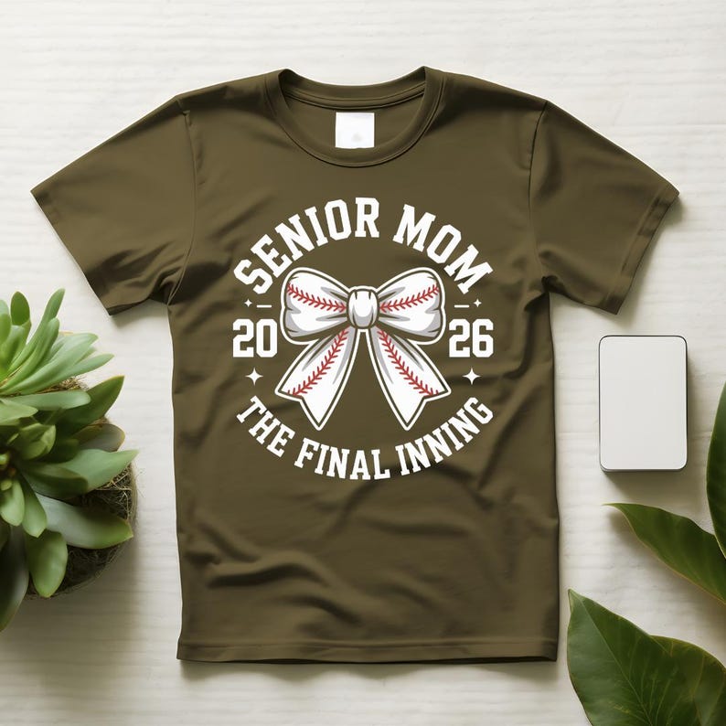 Może przedstawiać: Zielona koszulka z białym motywem baseballowym. Grafika zawiera napisy "Senior Mom 2026" i "The Final Inning" otaczające kokardę w kształcie piłki do baseballu.