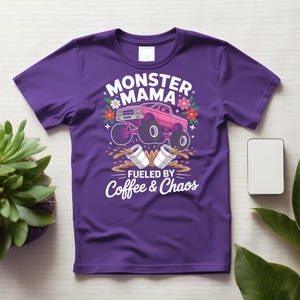 May include: Purple t-shirt with a graphic design featuring a pink monster truck, flowers, and the words "MONSTER MAMA" and "FUELED BY Coffee & Chaos" in white. The design includes coffee cups and splashes.