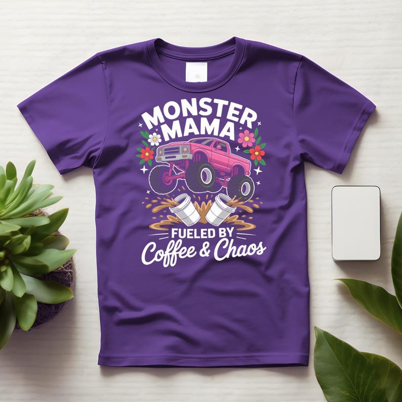 May include: Purple t-shirt with a graphic design featuring a pink monster truck, flowers, and the words "MONSTER MAMA" and "FUELED BY Coffee & Chaos" in white. The design includes coffee cups and splashes.
