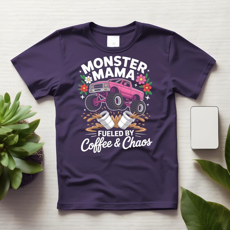 May include: A purple t-shirt featuring a pink monster truck graphic with the words "MONSTER MAMA" and "FUELED BY COFFEE & CHAOS". The design includes flowers and coffee cups.