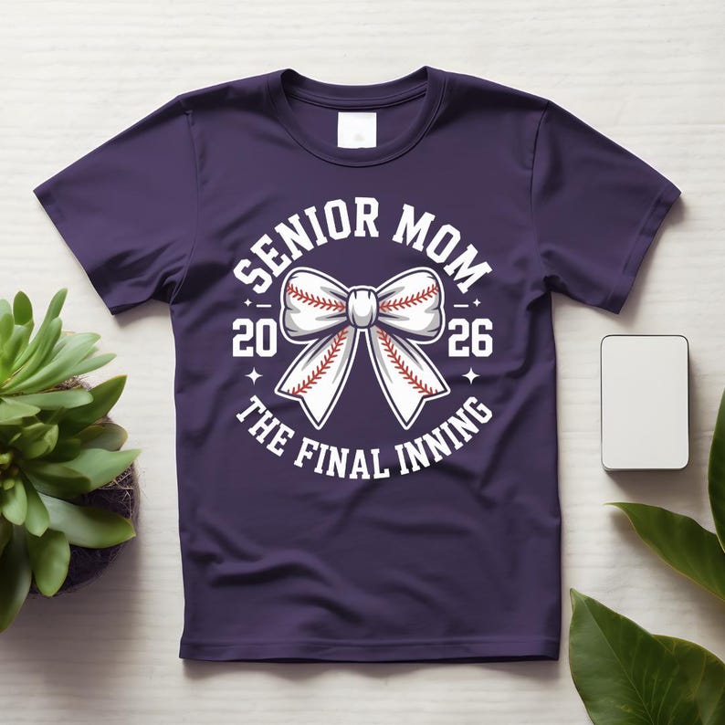 Może przedstawiać: Fioletowa koszulka z białą grafiką. Grafika zawiera słowa "Senior Mom" nad liczbami "20 26" i słowa "The Final Inning" poniżej. W środku znajduje się wz&oacute;r kokardy z motywem baseballowym.