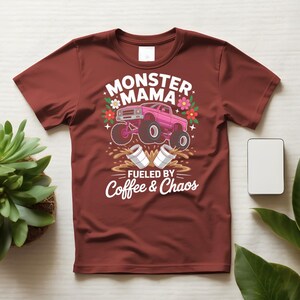 May include: A maroon t-shirt featuring a graphic design. The design includes the words "MONSTER MAMA" above a pink monster truck illustration. Below the truck, the text reads "FUELED BY Coffee & Chaos". Floral and coffee cup graphics complete the design.