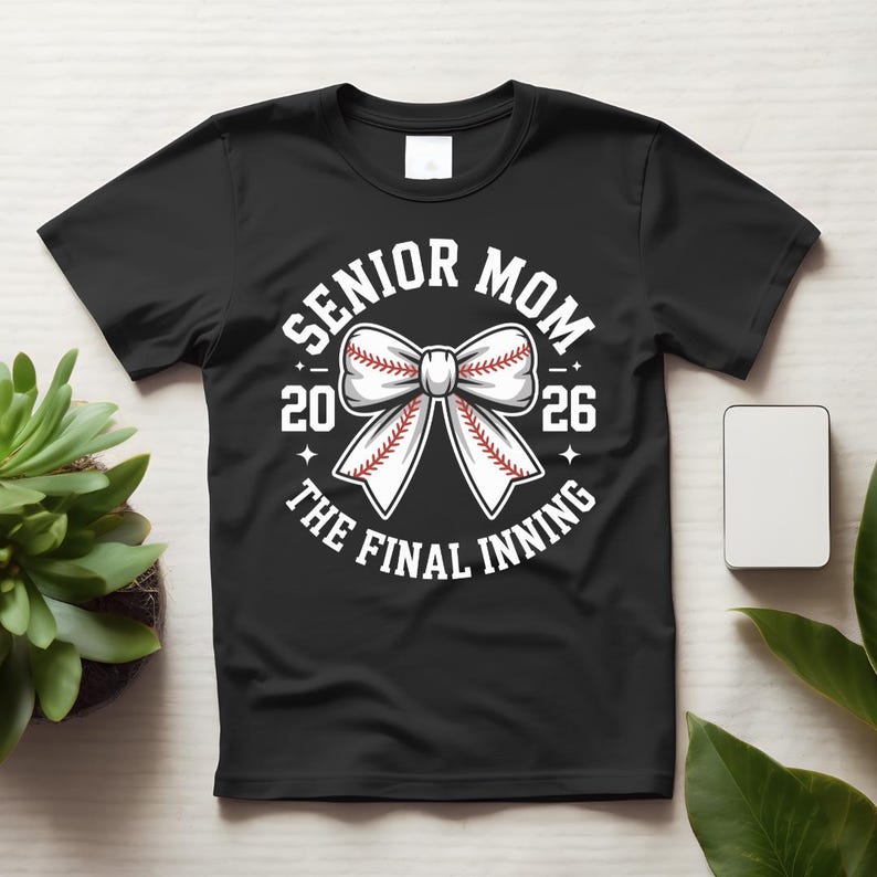 Może przedstawiać: Czarna koszulka z białym wzorem kokardy w stylu baseballowym. Tekst brzmi "SENIOR MOM 2026 THE FINAL INNING". Projekt zawiera piłkę do baseballu z czerwonymi szwami i gwiazdami.