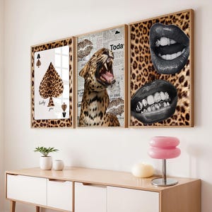 May include: A triptych of framed art prints. The prints display a leopard print background with a playing card, a roaring leopard, and two sets of lips. The frames are a light brown colour.