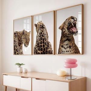 Puede incluir: Tres impresiones artísticas enmarcadas con leopardos. Las impresiones muestran leopardos en varias poses, incluido uno bostezando. Los marcos son de color madera clara y el fondo es blanco. Las impresiones se exhiben encima de un mueble de madera clara.