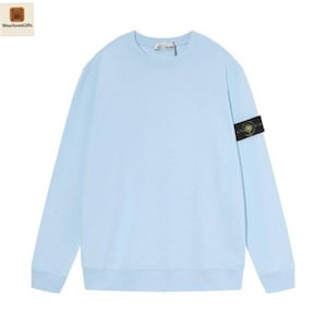 Könnte beinhalten: Hellblaues Sweatshirt mit Rundhalsausschnitt. Das langärmlige Oberteil hat ein kleines Logo auf der Brust und einen schwarz-gelben Aufnäher am linken Ärmel. Das Sweatshirt ist aus weichem Material.