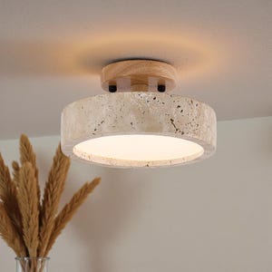May include: A modern ceiling light fixture with a round, textured stone shade and a wooden base. The light emits a warm glow, perfect for interior lighting. The fixture is designed for ceiling mounting.