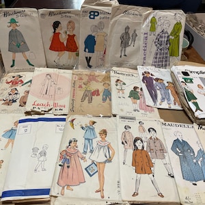May include: A collection of vintage paper sewing patterns featuring various illustrations of children's clothing, including dresses, coats, and pyjamas. The envelopes display brand names like Blackmere, Butterick, New Look, Simplicity, and Maudella.