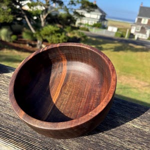 Pu&ograve; includere: Una ciotola di legno fatta a mano, di colore marrone scuro con venature del legno visibili. La ciotola ha un interno liscio e lucido e un bordo leggermente angolato. Questa ciotola decorativa &egrave; perfetta per servire o esporre.