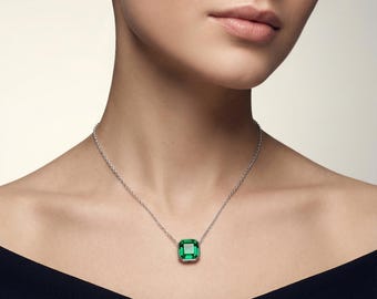 Könnte beinhalten: Eine silberne Halskette mit einem quadratischen, smaragdgrünen Edelsteinanhänger. Der Anhänger ist in einen silbernen Rahmen gefasst und hängt an einer feinen Silberkette. Die Halskette wird von einer Person mit einem schwarzen Oberteil getragen.