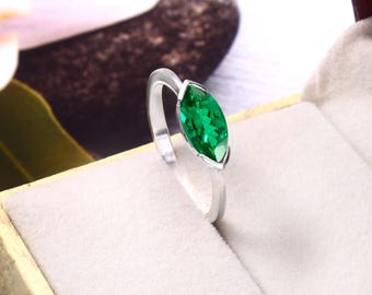 May include: A silver ring featuring a marquise-cut, vibrant green gemstone. The gemstone is set in a sleek, minimalist design, presented in a jewelry box. The ring's band is thin and polished, highlighting the emerald-like stone.