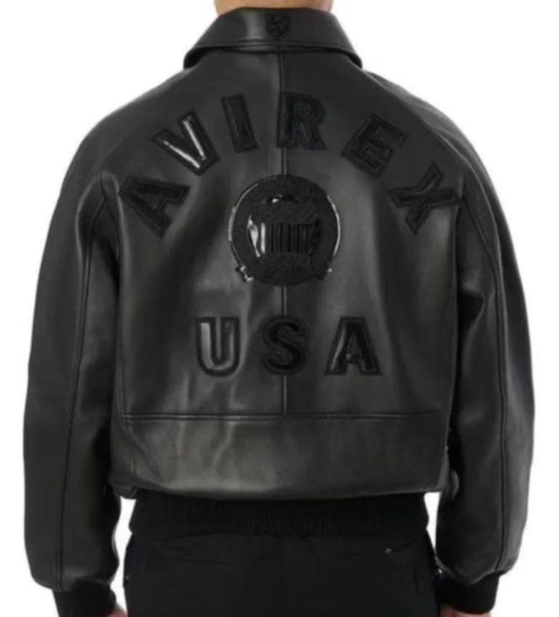 May include: Black leather jacket featuring the word "AVIREX" across the shoulders and "USA" below. The jacket has a ribbed hem and cuffs. A circular emblem is centered between the words. The jacket is a classic bomber style.