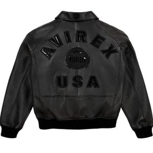 May include: Black leather jacket featuring the word "AVIREX" arched across the upper back, with a circular emblem and "USA" below. The jacket has a ribbed collar, cuffs, and hem. The jacket is a bomber style.