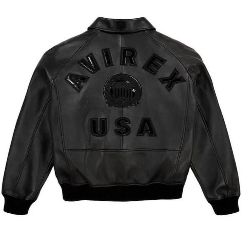 May include: Black leather jacket featuring the word "AVIREX" arched across the upper back, with a circular emblem and "USA" below. The jacket has a ribbed collar, cuffs, and hem. The jacket is a bomber style.
