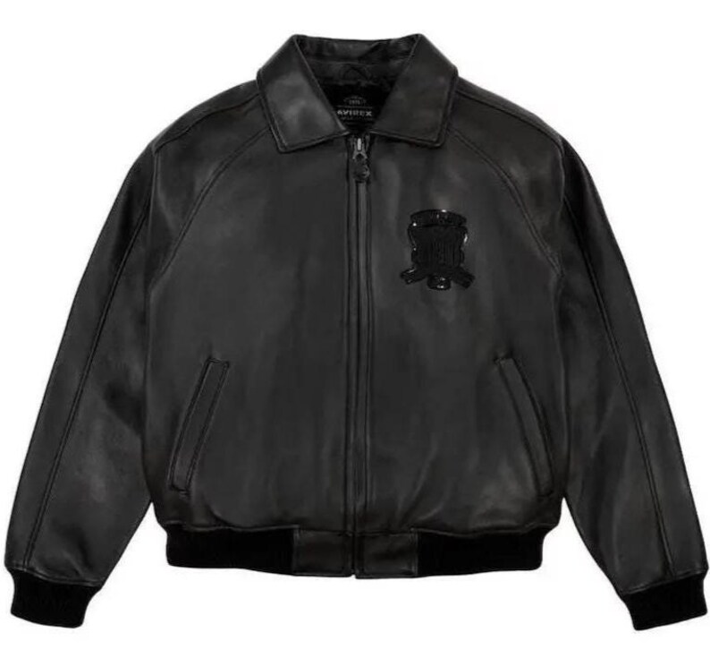 May include: Black leather bomber jacket with a collared neckline, zip closure, and ribbed cuffs and hem. Features a decorative emblem on the chest. The jacket has two front pockets.