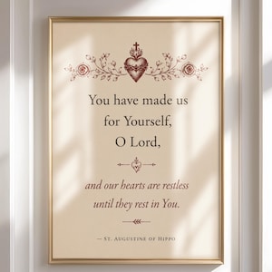 Op de afbeelding: Een ingelijste kunstdruk op een crèmekleurige achtergrond met de tekst: You have made us for Yourself, O Lord, and our hearts are restless until they rest in You. - St. Augustine of Hippo. Boven de tekst staat een rode illustratie van het Heilig Hart.
