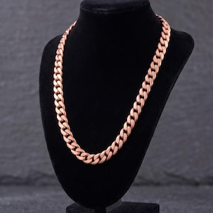 May include: A rose gold-toned cuban link chain necklace featuring a series of interlocking, flattened oval links. The metal surface has a polished, reflective finish that catches the light, creating a uniform appearance across the entire length.