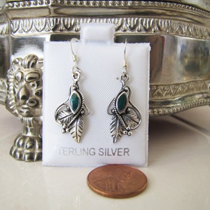 May include: A pair of sterling silver earrings with a leaf and oval green stone design. The earrings are displayed on a white card with the words "STERLING SILVER" printed on it. A penny is in the foreground.
