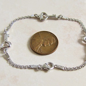 May include: A silver-toned chain bracelet featuring three heart-shaped key charms spaced evenly along the links. The bracelet includes a lobster claw clasp and is shown next to a copper-colored United States penny for scale reference.