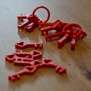 Könnte beinhalten: Eine Sammlung leuchtend roter Schlüssel, einige mit Schlüsselringen, liegt auf einer Holzoberfläche. Die Schlüssel haben ein detailliertes, strukturiertes Design, und die Beleuchtung erzeugt Schatten, die ihre Formen hervorheben. Die Schlüssel sind der Blickfang vor dem warmen Holzmaserungshintergrund.