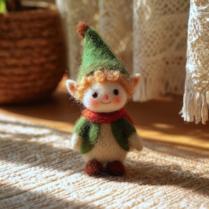 May include: A handcrafted felt elf doll with a green hat and jacket, a red scarf, and brown shoes. The doll has a smiling face with rosy cheeks and curly orange hair. The elf is standing on a beige rug.