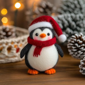 May include: A handmade felt penguin figure wearing a red Santa hat and scarf. The penguin has a white belly, black wings, and orange feet. A festive Christmas decoration.