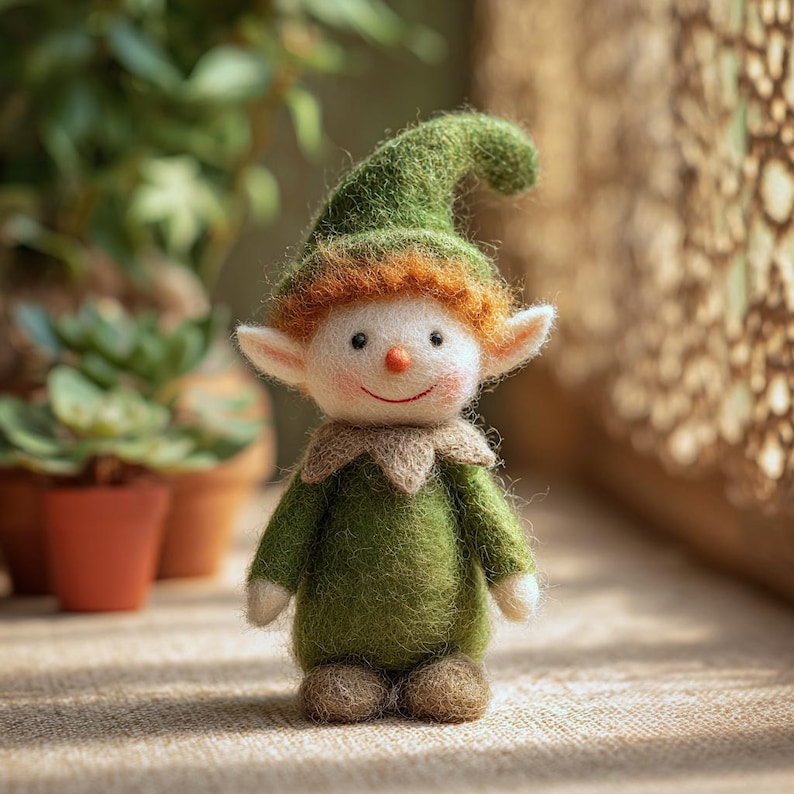 May include: A handcrafted felt elf doll with a green hat and outfit, red hair, and a smiling face. The doll has white ears, a tan collar, and brown feet. It is standing on a textured surface with plants in the background.