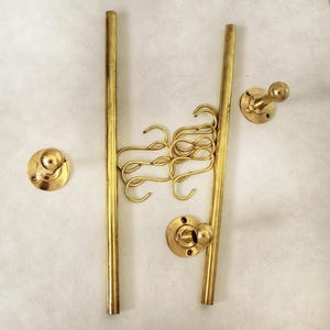 May include: A collection of brass-colored hardware components, including two vertical rods, several S-shaped hooks, and three wall-mounted knobs. The components are arranged against a neutral background, suggesting a display or organizational system.