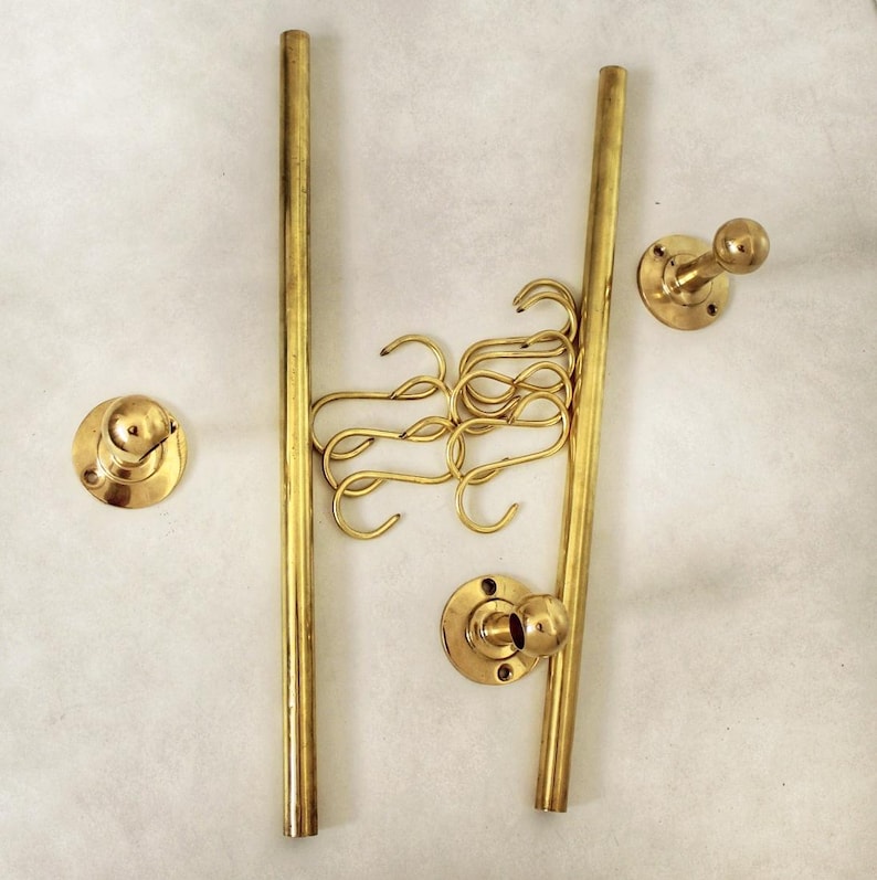 May include: A collection of brass-colored hardware components, including two vertical rods, several S-shaped hooks, and three wall-mounted knobs. The components are arranged against a neutral background, suggesting a display or organizational system.