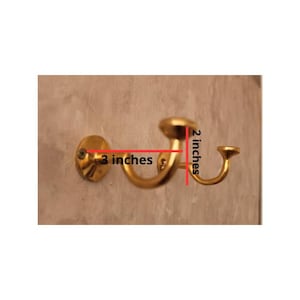 May include: A gold-colored wall hook, 3 inches wide and 2 inches high, mounted on a wall. The hook has a curved design with a circular base and a rounded top. The hook is designed for hanging items.