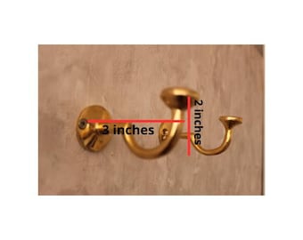 May include: A gold-colored wall hook, 3 inches wide and 2 inches high, mounted on a wall. The hook has a curved design with a circular base and a rounded top. The hook is designed for hanging items.