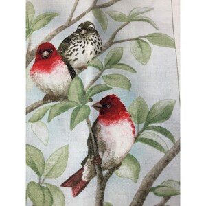 May include: A fabric print featuring three birds perched on brown tree branches with green leaves. Two birds have bright red heads and white chests, while the third bird is brown with dark spots. The background is a light, pale blue color.