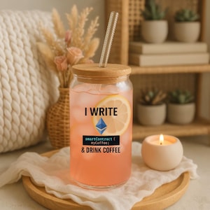 Peut inclure: Un verre transparent avec un couvercle en bambou et une paille transparente, rempli d'une boisson rose et d'une tranche de citron. Le texte "I WRITE & DRINK COFFEE" est imprimé sur le verre. Le verre est sur un plateau en bois.