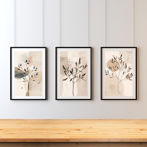 May include: Three framed art prints with abstract botanical designs. Each print has a black frame and features a stylized tree branch against a neutral background with soft colour washes in beige, grey, and pink.