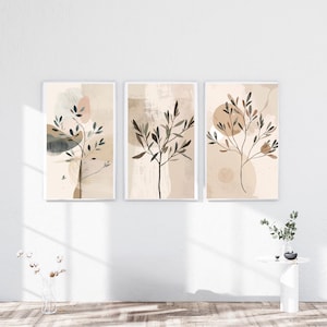 May include: Three framed botanical art prints. Each print features a minimalist design of a tree branch with leaves in shades of brown and green against a neutral background with abstract shapes. The frames are white, and the overall aesthetic is modern and serene.