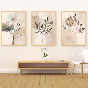 May include: Three framed abstract art prints with botanical designs. Each print features a tree branch with leaves in shades of brown and black against a neutral background with beige and pink accents. The frames are light wood.