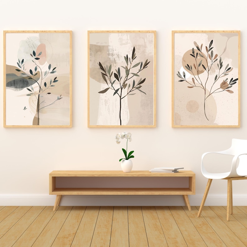 May include: Three framed abstract art prints with botanical designs. Each print features a tree branch with leaves in shades of brown and black against a neutral background with beige and pink accents. The frames are light wood.