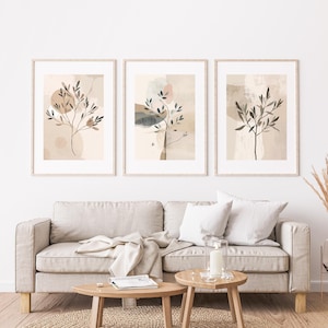 May include: Three framed abstract art prints with botanical designs. Each print features a stylized tree with leaves against a neutral background with soft colour blocks in beige, brown, and muted tones. The frames are light wood.