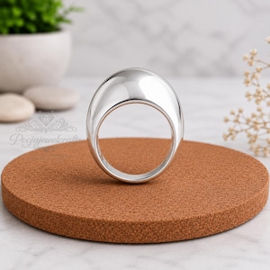 May include: A polished silver-tone ring with a smooth, rounded, dome-shaped top and a circular band. The ring features a reflective, metallic surface and is positioned upright. The text "Poojajewelcrafts" is visible on the left side of the image.
