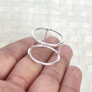 May include: A silver ring with a geometric design. The ring has two parallel oval bands connected by vertical bars, creating an open, cage-like structure. The ring is made of shiny, polished metal.